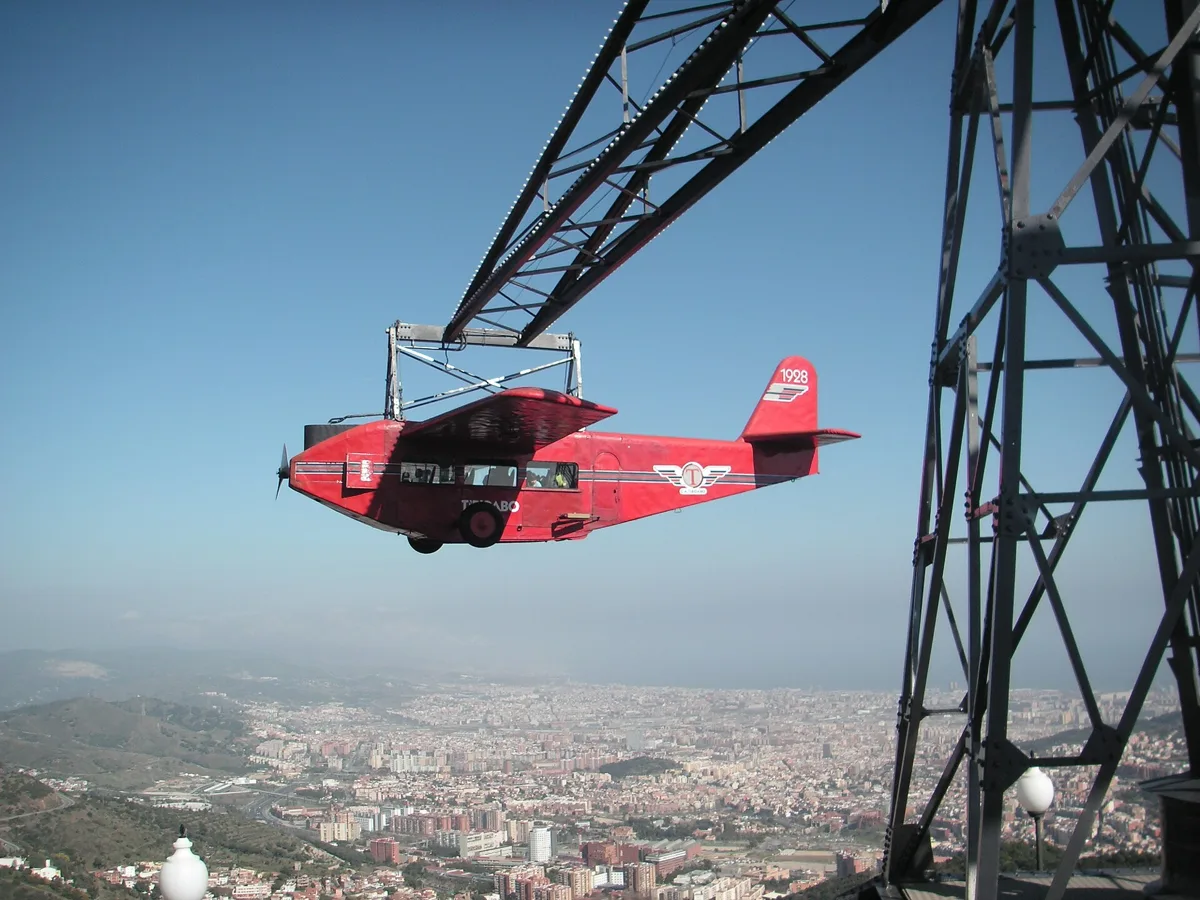 The Avió ride at Tibidabo, a red replica plane hanging from a metal arm with Barcelona below