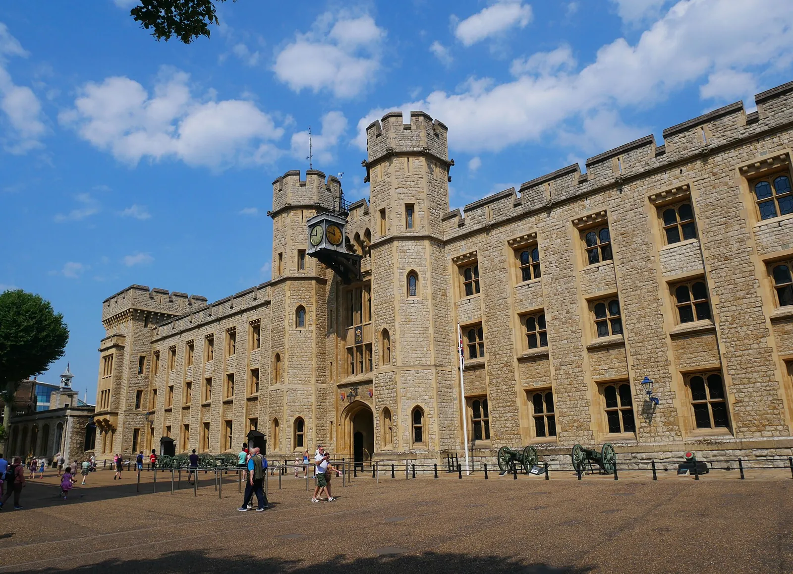 The Waterloo Block of the Tower of London, a long crenellated stone building with towers and a clock on the tower beside the entrance, with visitors in the courtyard