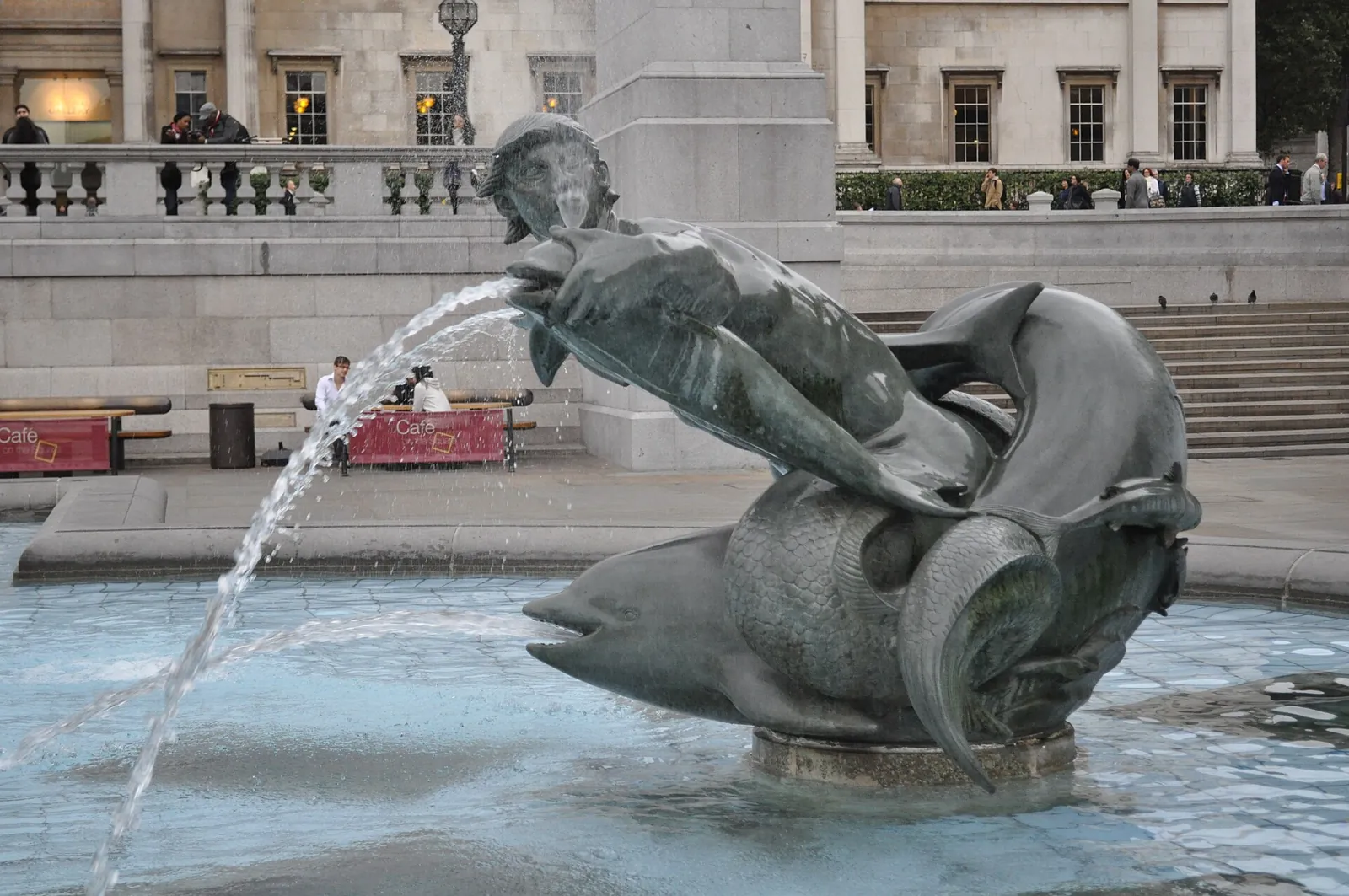 Bronze sculpture of a triton with a dolphin in the pool of one of the fountains, spouting a jet of water