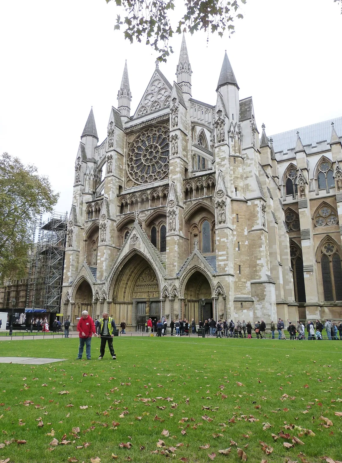 The north front of Westminster Abbey with its rose window and the North Door, with a line of visitors queuing along the wall